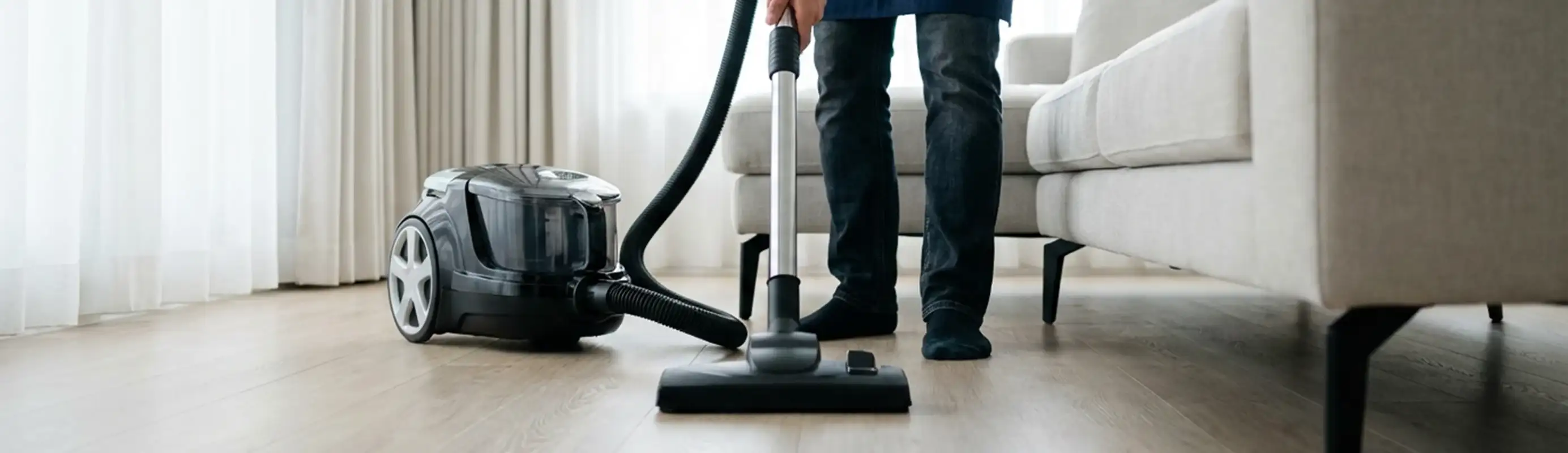 Professional house cleaner vacuuming a living room floor with a canister vacuum cleaner, Chicago, IL.