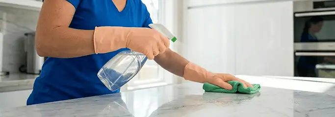 Maid service worker spraying and wiping a kitchen countertop with a microfiber cloth for sanitizing, Chicago, IL.
