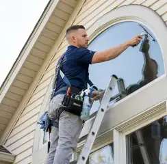 Professional window cleaner on a ladder using a squeegee to clean an exterior arched window, Chicago, IL.