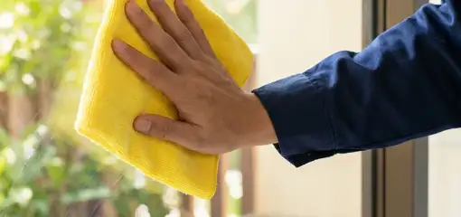 House cleaner wiping a glass window with a yellow microfiber cloth for streak-free cleaning, Chicago, IL.